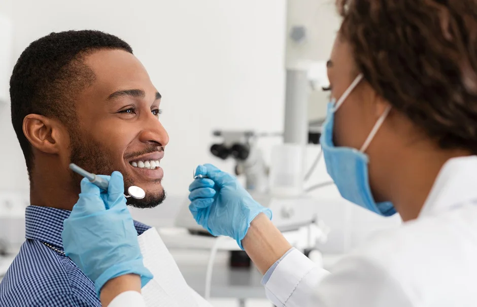 Dentist examining smiling male patient with dental tools
