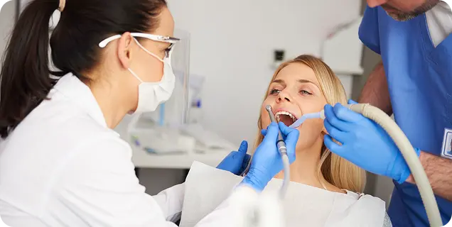 A dentist and assistant performing a dental procedure on a female patient in a dental clinic