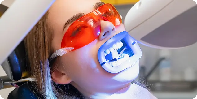 A patient wearing orange protective glasses undergoing professional teeth whitening treatment with a UV light device