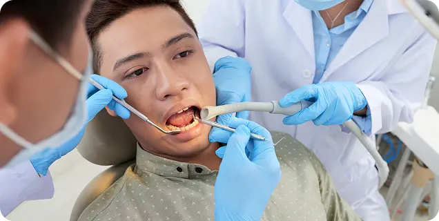 Two dental professionals in gloves performing a tooth extraction procedure on a male patient