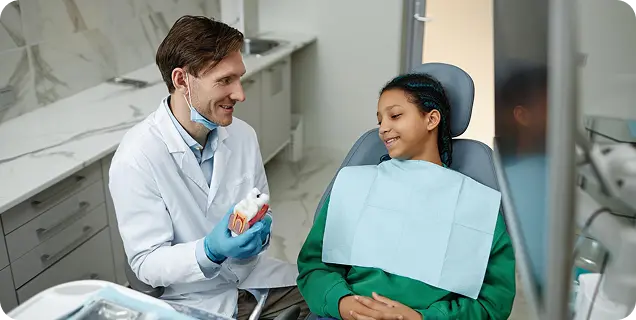 A dentist showing a dental model to a young girl patient in a dental chair
