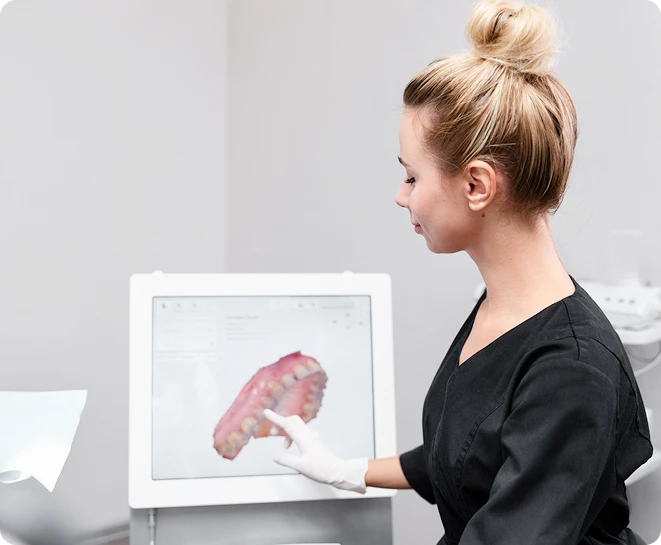 Dental professional in black scrubs reviewing a 3D digital dental scan on a touchscreen monitor in a clinic