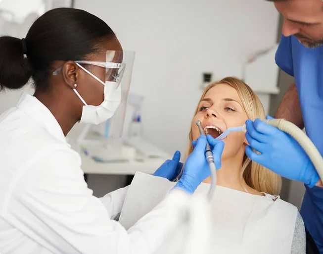 Two dental professionals in gloves and protective gear performing a procedure on a female patient in a dental chair