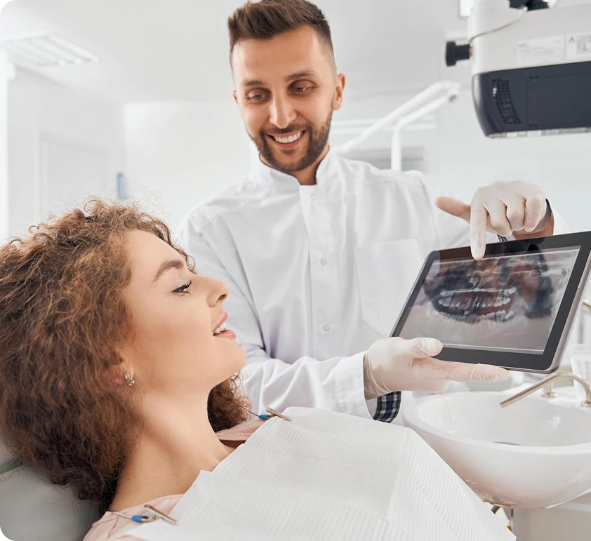 Smiling dentist showing a dental X-ray on a tablet to a female patient reclining in a dental chair