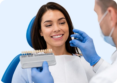 Dentist holding a tooth shade guide next to a smiling female patient in a dental chair for a teeth whitening consultation