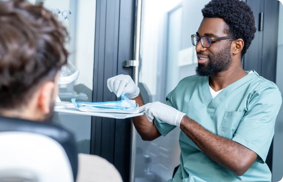 Gloved dental professional preparing sterile instruments beside a patient