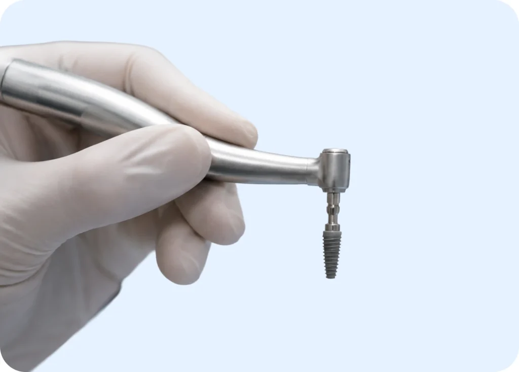 Gloved hand holding a dental drill with a titanium implant screw for placement